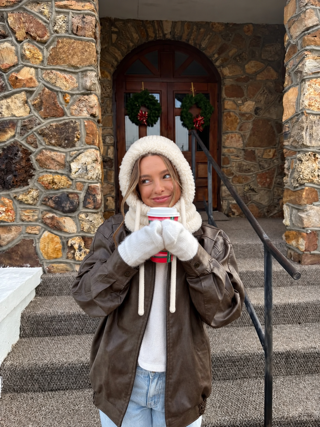 Ivory 3-in-1 plush beanie worn with a brown leather jacket and coffee outside a stone doorway